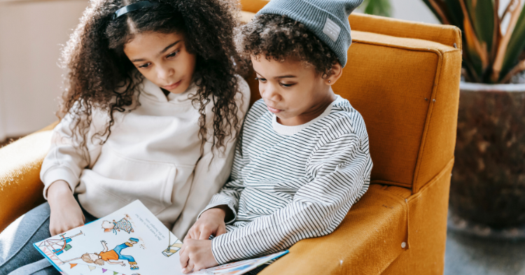 two kids sitting in an orange chair reading a book.